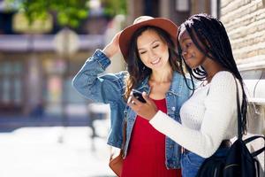 dos amigos mirando su teléfono inteligente juntos. mujeres multiétnicas. foto