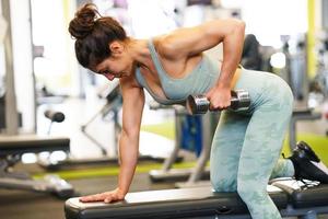 Mujer trabajando en sus tríceps y bíceps en un gimnasio con mancuernas foto