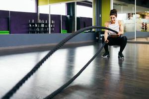 Young and athletic woman using training ropes in a gym.