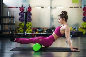 Mujer relaja los músculos de las piernas con un rodillo de espuma verde foto