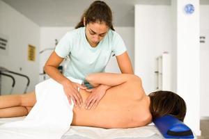 Professional female physiotherapist giving lumbar shoulder massage to a woman