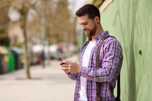 Smiling young man looking his smart phone in urban background. Lifestyle concept. photo