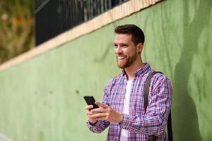 Young man laughing with his smart phone in urban background. Lifestyle concept.