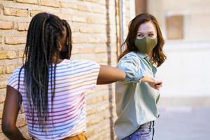 Multiethnic young women wearing masks greeting at each other with their elbows photo