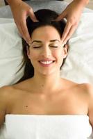 mujer sonriente joven que recibe un masaje de cabeza en un centro de spa.