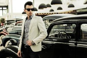 Young handsome man, model of fashion, wearing jacket and shirt with old cars photo