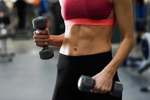 Young woman with beautiful abdomen lifting dumbells at gym photo