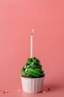 Christmas tree shaped cupcake with a candle on pink background photo