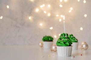 Christmas tree shaped cupcakes, surrounded with festive decorations and lights on the background photo