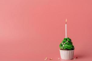 Christmas tree shaped cupcake with a candle on pink background photo