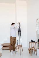 Fotógrafo masculino que trabaja en un interior minimalista, luminoso y aireado, silla, alfombra y almohadas blancas y beige foto