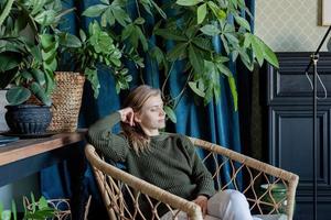 Joven mujer rubia sentada en una silla cómoda rodeada de plantas