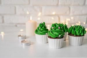 Christmas tree shaped cupcakes, surrounded with festive decorations and lights on the background photo