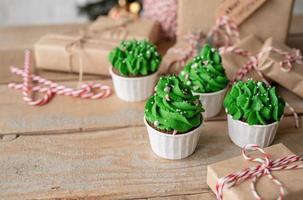 Christmas tree shaped cupcakes, surrounded with festive decorations and lights on the background photo