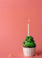 Christmas tree shaped cupcake with a candle on pink background photo