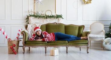 Mujer joven tumbado en el sofá solo en un salón decorado para Navidad