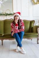 Mujer joven sentada en el sofá solo en un salón decorado para Navidad