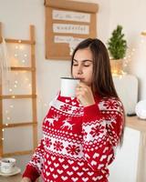 Happy young woman in christmas sweater making hot drinks in the kitchen