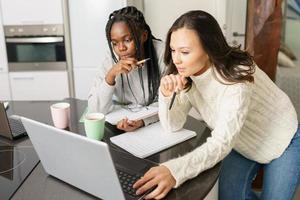 Dos chicas universitarias que estudian juntas en casa con computadoras portátiles mientras beben café