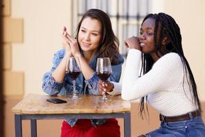 Two women drinking red wine sitting at a table outside a bar. photo