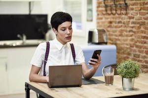 Young businesswoman with very short haircut looking at her smartphone at home. photo