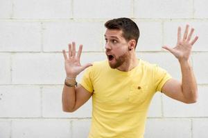 Funny young man on brick wall with open hands looking at leftside. photo