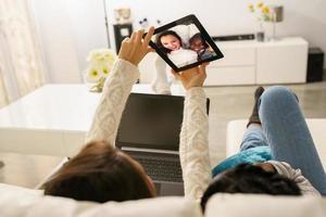 Two female friends making a selfie with a digital tablet sitting on the couch at home. photo