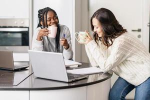 Dos chicas universitarias que estudian juntas en casa con computadoras portátiles mientras beben café