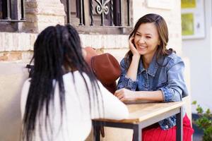 Two multiethnic friends talking sitting at a table outside a bar. photo