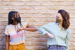 Mujeres jóvenes multiétnicas con máscaras saludándose con los codos foto