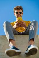 Young man using his smartphone sitting on a ledge outside photo