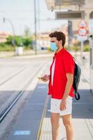 Young man wearing a surgical mask while waiting for a train at an outside station photo