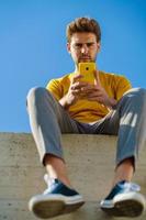 Man using his smartphone sitting on a ledge outside
