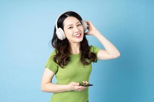 Asian grasshopper girl portrait is listening to music, isolated on blue background photo