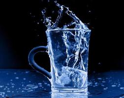 Resumen de salpicaduras de vidrio de botella transparente de agua azul con burbujas en negro. foto