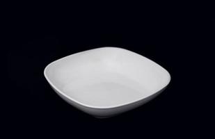 a single white plate isolated on a black background. utensil shot from front point of view. disposable dishware for graphics and mockup use. photo