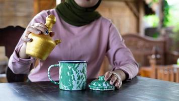a lady pours a drink on her ethnic cup at a traditional vibes restaurant. summer vibes in Indonesia.