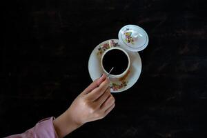 una taza de café caliente está sobre la mesa. una niña tiene una bebida sabrosa en la mano. una especie de disfrute del tiempo libre. foto