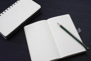 black desk with notebook and pencil on top of it. a notebook mockup on desk as a workspace layout. office object isolated on black background. photo