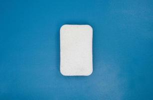Esponja de melamina blanca sobre fondo azul. Herramienta de limpieza doméstica para uso diario. Accesorio para lavavajillas en casa.