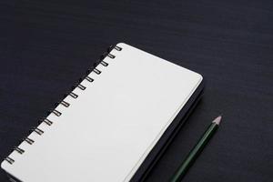 black desk with notebook and pencil on top of it. a notebook mockup on desk as a workspace layout. office object isolated on black background. photo