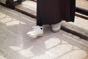 the feet of a woman wearing a black skirt and white shoes. she may take a step to move from her position. photo