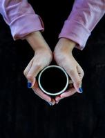 una taza de café caliente está sobre la mesa. una niña tiene una bebida sabrosa en la mano. una especie de disfrute del tiempo libre. foto