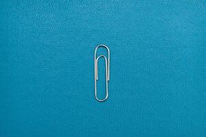 silver paper clip on blue background. realistic paperclip for binding paper and notes. silver metal fastener for office stationery. photo