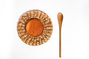 a wooden placemat on top of the wicker placemat and a wooden spoon beside on white. a flat lay shot of the organic utensils. a serving concept. photo