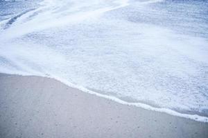 la ola de espuma en la playa de arena. olas suaves en la costa que se siente tranquila y agradable para relajarse. foto