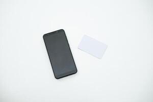 a blank black smartphone is next to the blank white card on the white table. a graphic source for mockup. photo