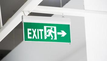 the exit route sign in green color is hanging on a white wall. the essential sign of the public places.