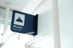 mushola direction or a prayer room sign is hanging on a white wall. the direction in a public place. photo