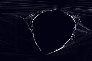 una envoltura de plástico transparente con un agujero sobre fondo negro. textura realista de envoltura de plástico rasgada para superposición y efecto. patrón de plástico arrugado para un diseño creativo y decorativo. foto